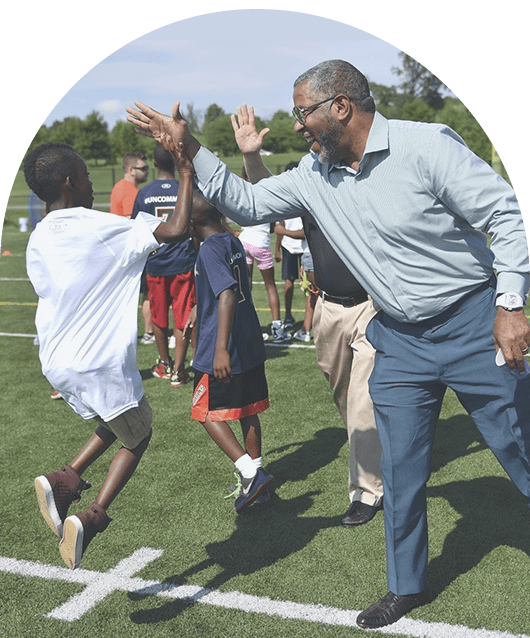 Businessman Robert F. Smith outside on a soccer field giving a kid a high five