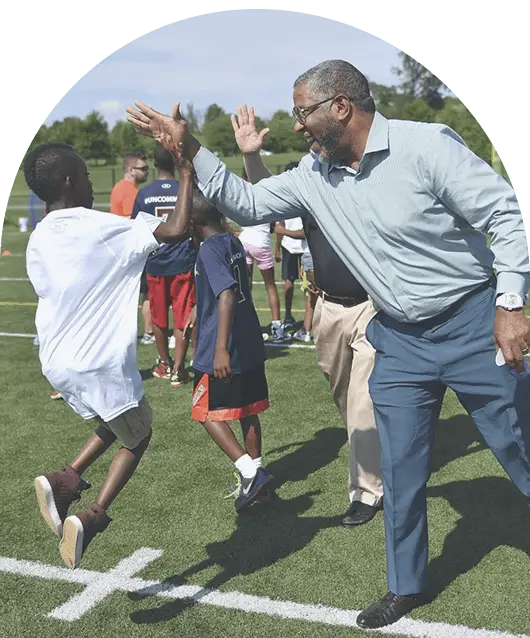 Businessman Robert F. Smith outside on a soccer field giving a kid a high five