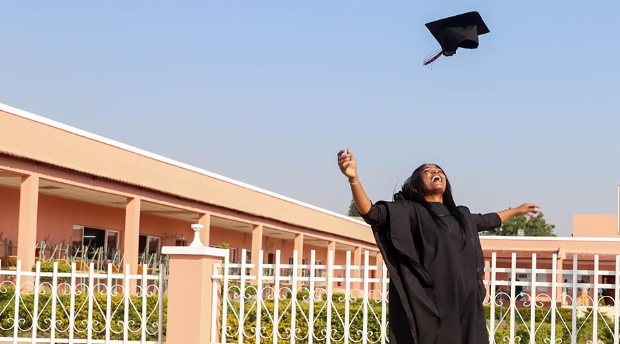 A young Black woman in a graduation gown throws her cap in the air