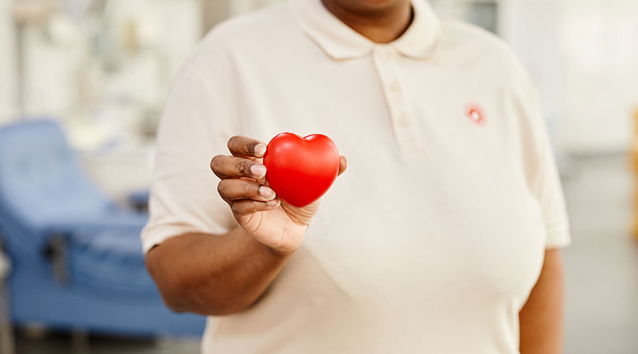 A Black woman stands holding a small red heart-shaped item.