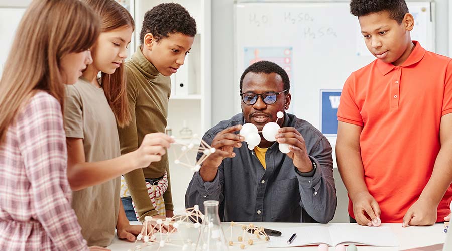 An African American STEM teacher shows his students a model in a classroom.