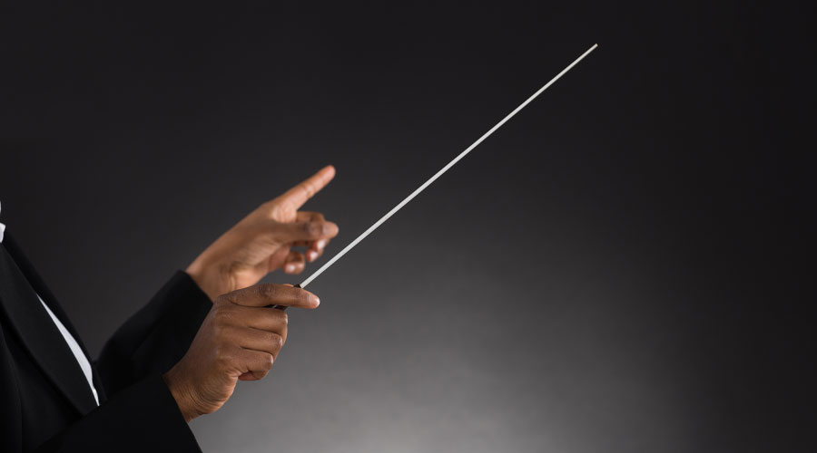 A pair of dark-skinned hands are shown with a conductor’s baton.