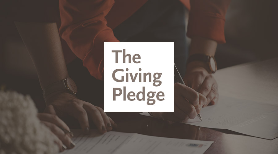 An image of two sets of hands signing a document is overlaid with the Giving Pledge logo.