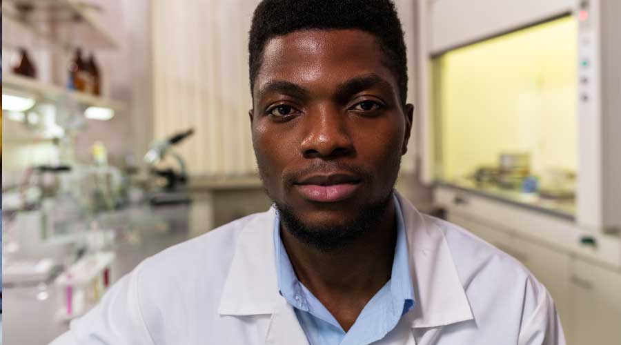 African American man in a white lab coat and blue collard shirt in a lab setting.
