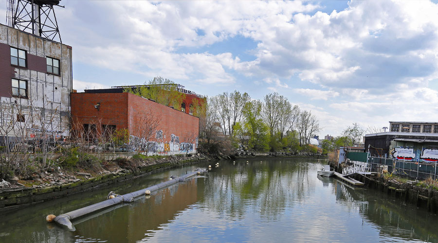 The Gowanus Canal surrounded by run-down buildings and trees.