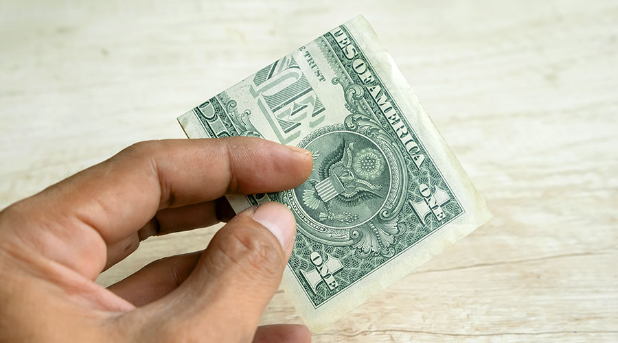 An up close picture of a hand holding a dollar bill folded.