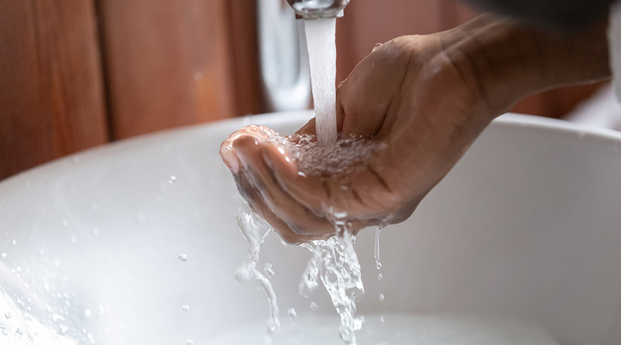 Image of a Black person holding their hand under a faucet with water running out of it