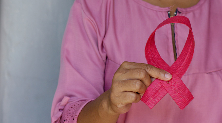 A woman wears all pink and holds a pink breast cancer awareness ribbon in her hand