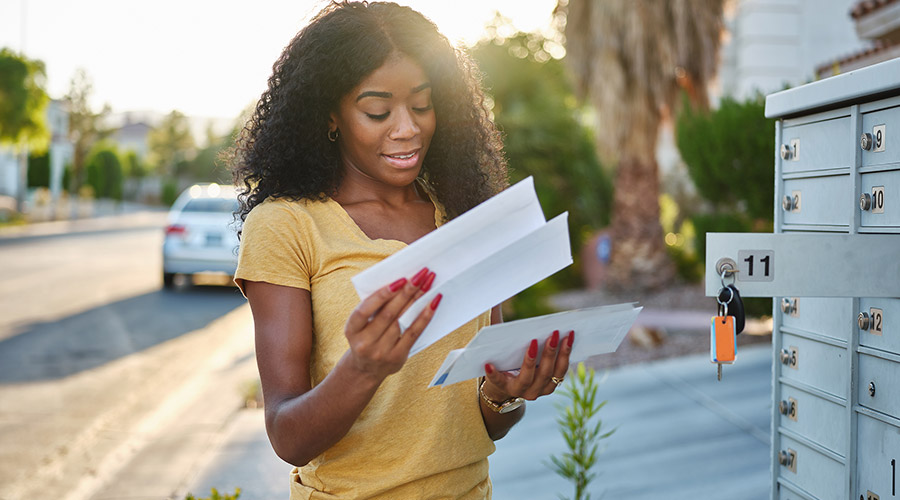 A young Black woman standing outside as she opens her mailbox to read letters