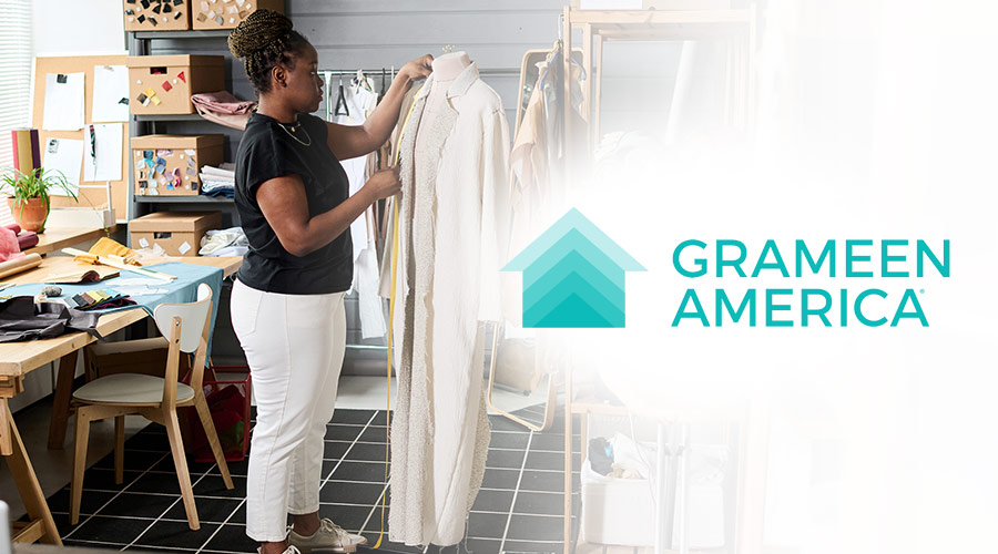 An image of a Black woman designing a coat on a mannequin with the logo of Grameen America placed to the right of the woman