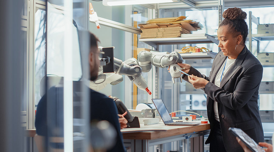 A Black woman inventor wearing a gray blazer while working on a robotic arm in a lab