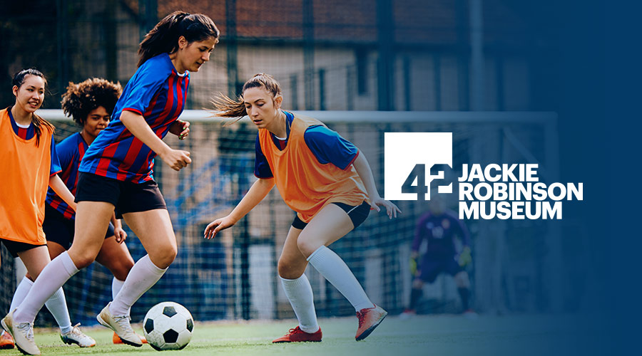 A group of women playing soccer with the Jackie Robinson Museum logo on the right side of the image