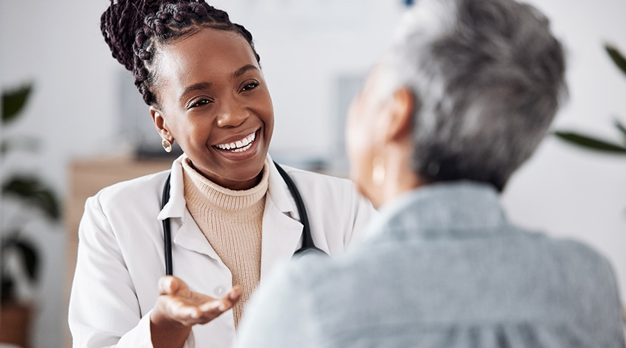 Black female doctor smiling while speaking with a patient in a doctor’s office