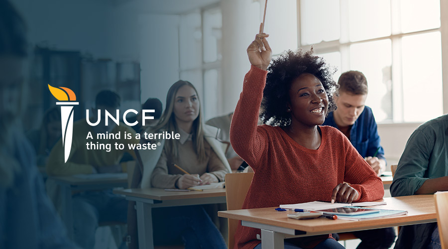 A black female college student raising her hand in class with the UNCF logo and motto on the left