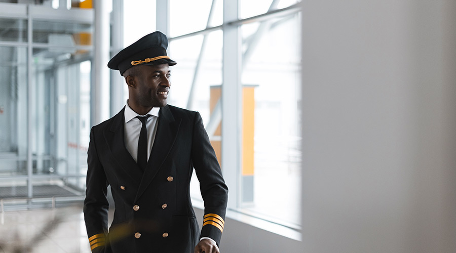 A uniformed Black pilot looking out of a window in an airport