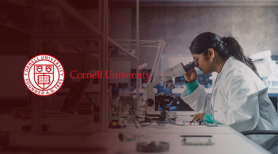 A student in a white lab coat in a lab at Cornell University with Cornell’s logo on the left