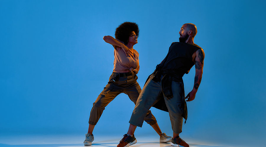 Two dancers facing each other in a performance space, smiling while doing dance poses