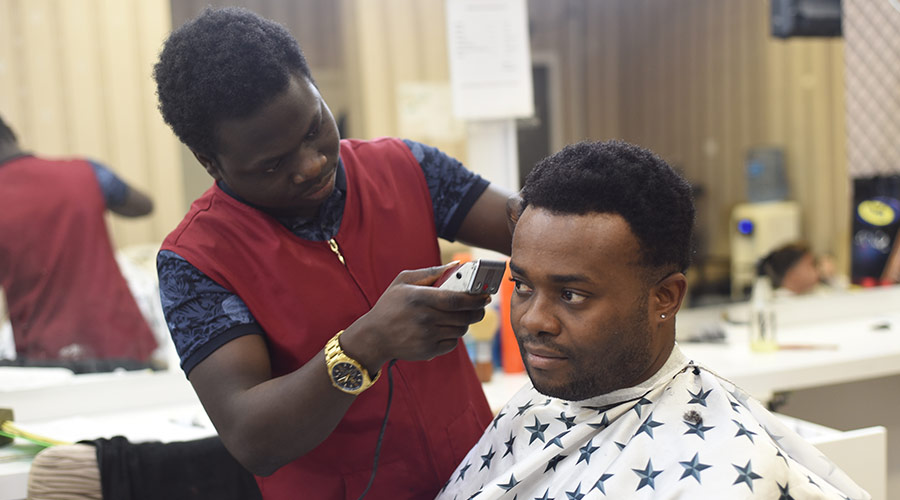 A barber cuts hair and stands beside a client sitting in a chair, who is wearing a white bib with blue stars