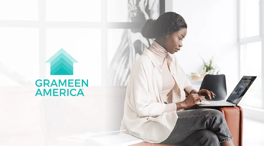 Black woman entrepreneur working on a laptop with the Grameen America logo