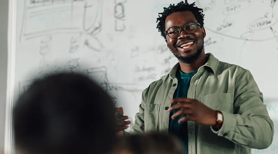 Man wearing a green button-up shirt and glasses, standing in front of a whiteboard