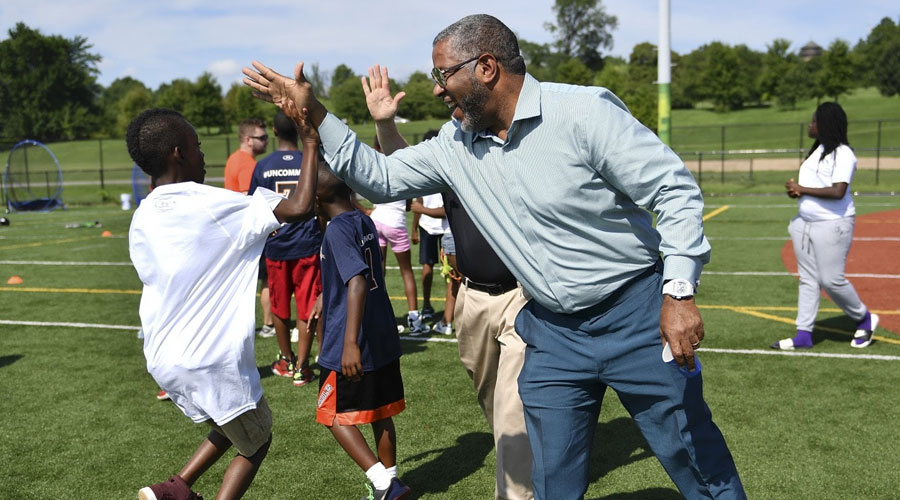Robert F. Smith stands on a sports field, sharing a high five with a young boy