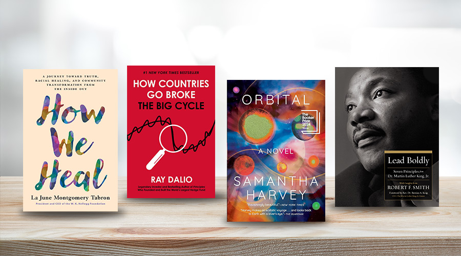 Four book covers are placed next to one another on a wooden desk