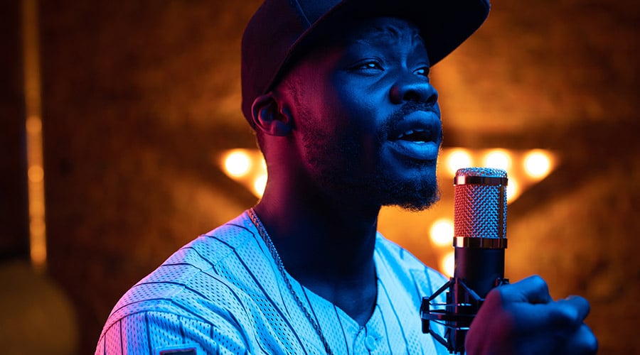 Man in a hat and striped jersey singing into a microphone.