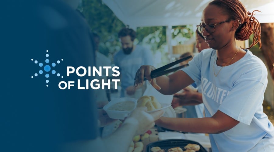 Volunteer serving food at a community event featuring the Points of Light logo